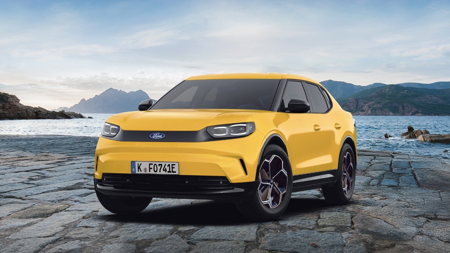 L’emblématique Ford Capri en jaune, photographiée devant un arrière-plan pittoresque d’eau et de montagnes.