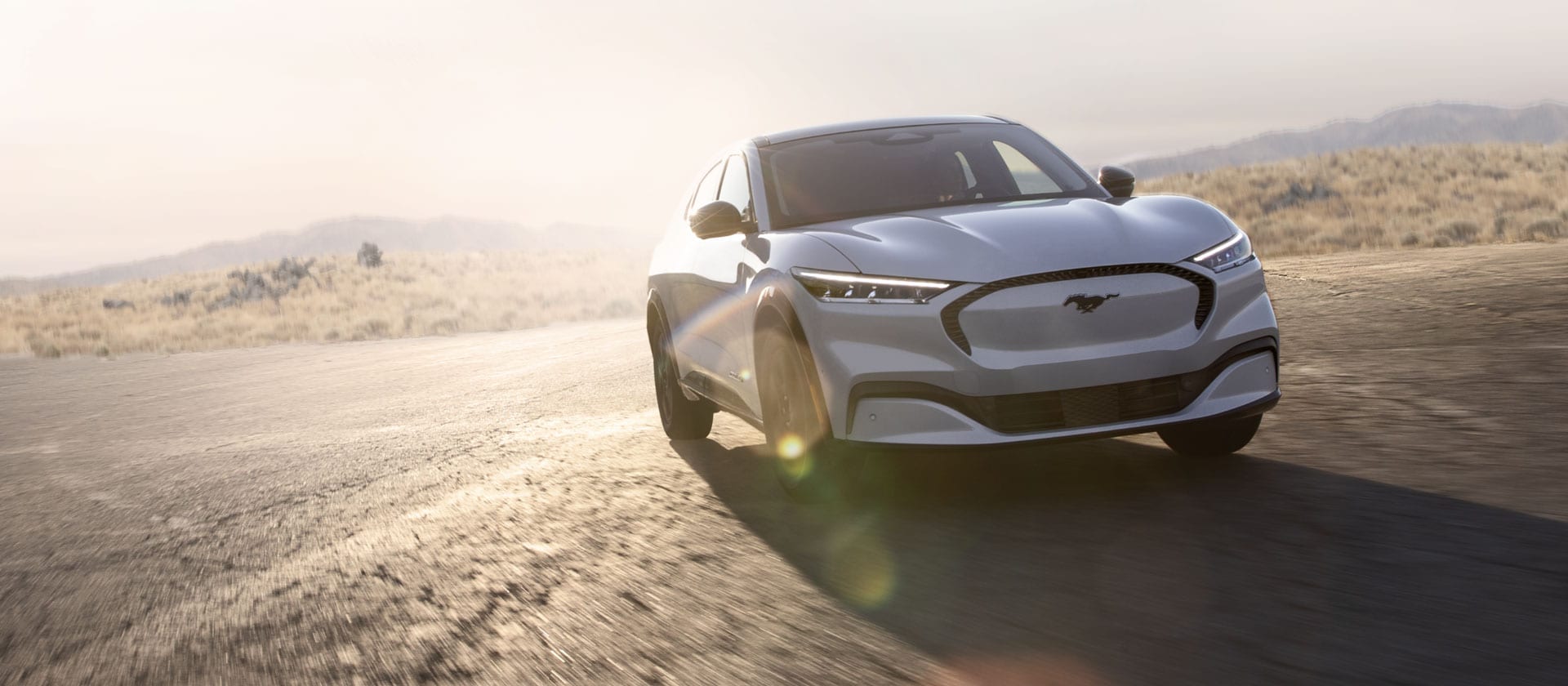 Une Ford Mustang Mach-E électrique de couleur argentée roule sur une longue route ouverte.