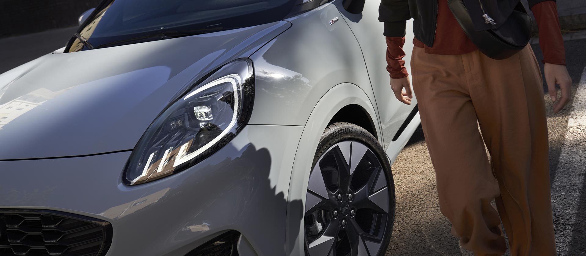Une personne se tient à côté d’une Ford Mustang Mach-E électrique de couleur argentée.