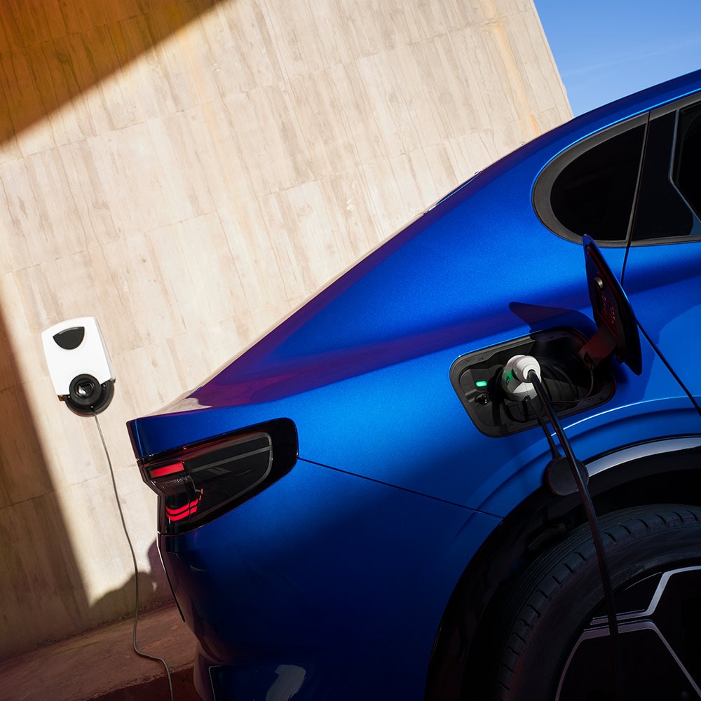 Vue arrière d’une Ford Capri électrique bleue branchée sur une borne de recharge.