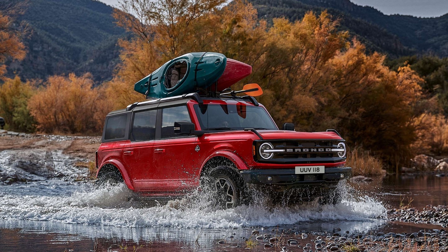 Ford Bronco en rouge. Vue de face de 3/4 dans un paysage rocheux traversant un cours d'eau