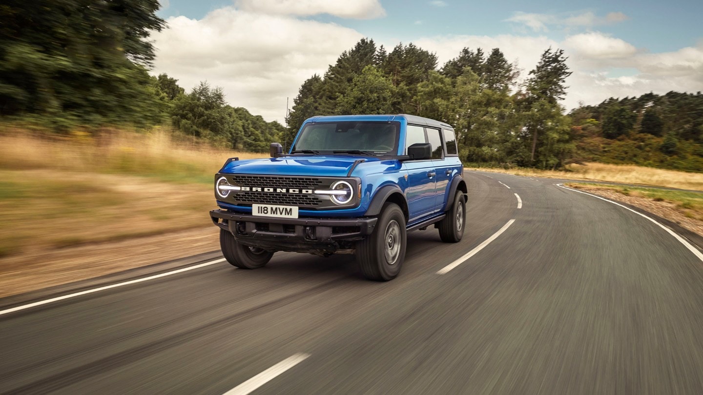 Ford Bronco en bleu en vue de face 3/4 roulant sur une route de campagne