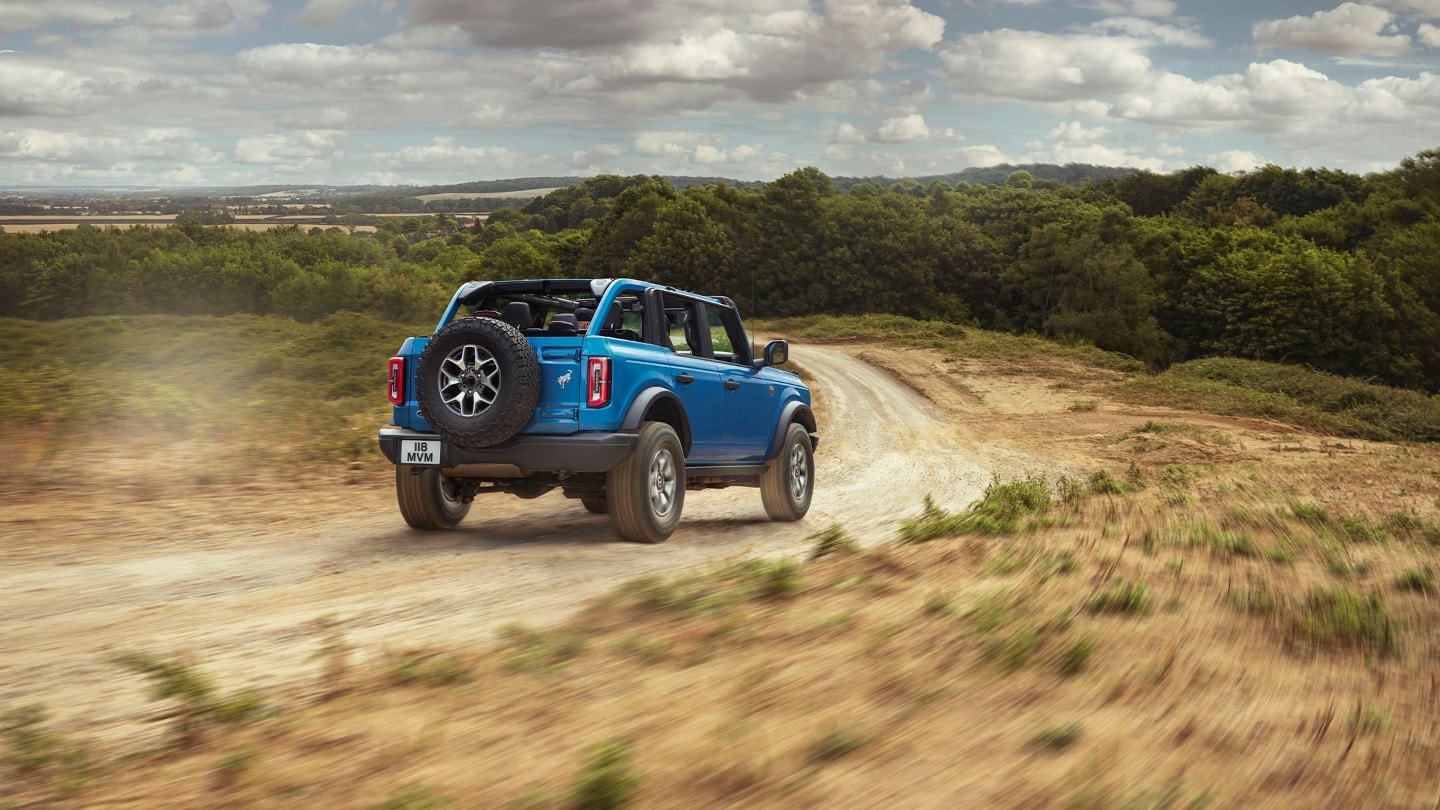 Ford Bronco en bleu, vue de 3/4 arrière. Conduisant sur un chemin de terre