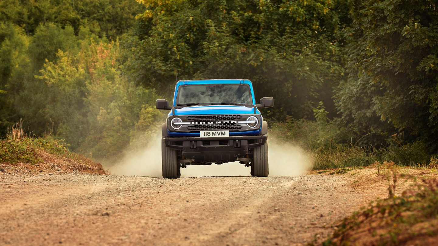 Ford Bronco en bleu, vue de face, roulant sur un chemin poussiéreux