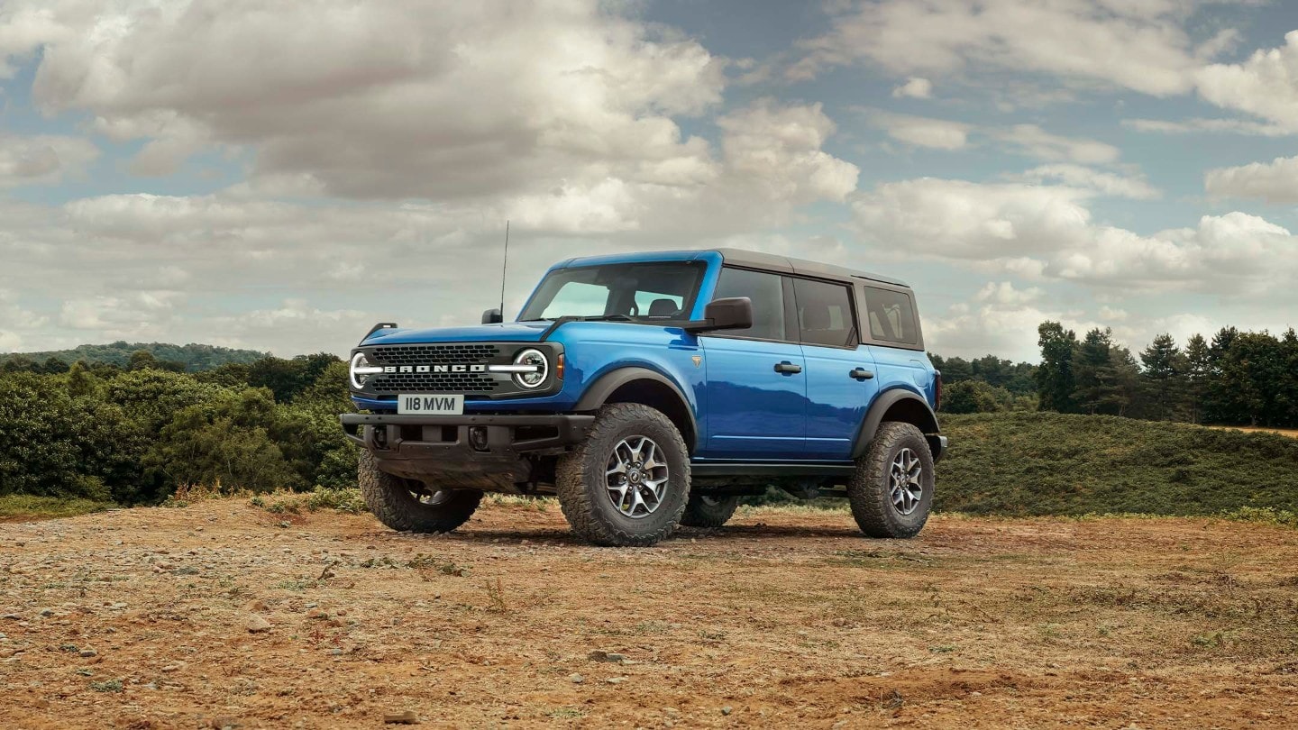 Ford Bronco en bleu, vue de face 3/4 debout sur un sol sableux