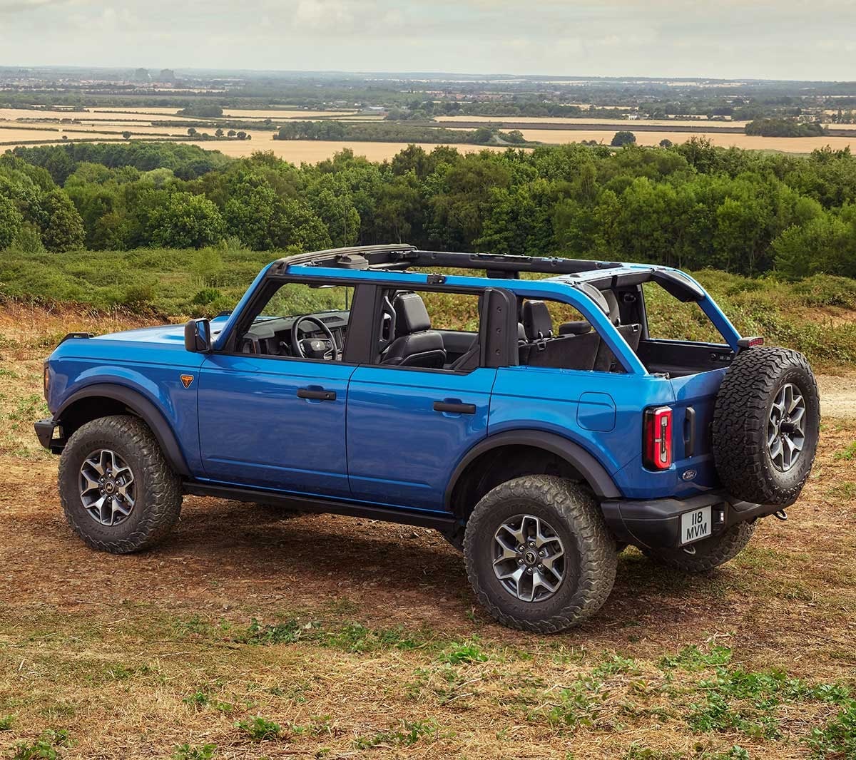 Ford Bronco en bleu, vue arrière 3/4 roulant sur un sol sablonneux