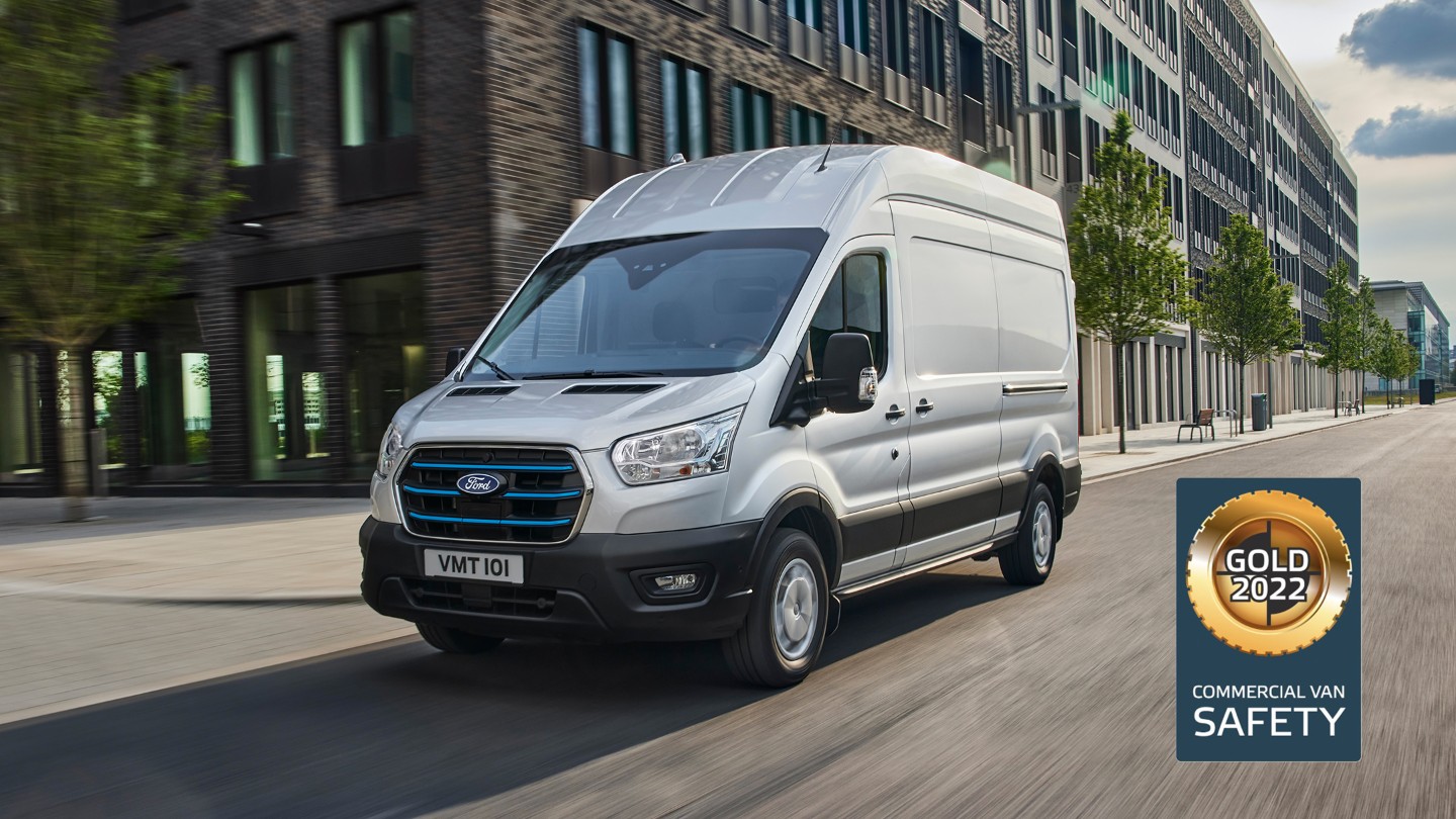 Ford E-Transit Fourgon couleur argent, vue latérale aux trois quarts, roulant le long de tours et logo NCAP Gold pour la catégorie «Sécurité»