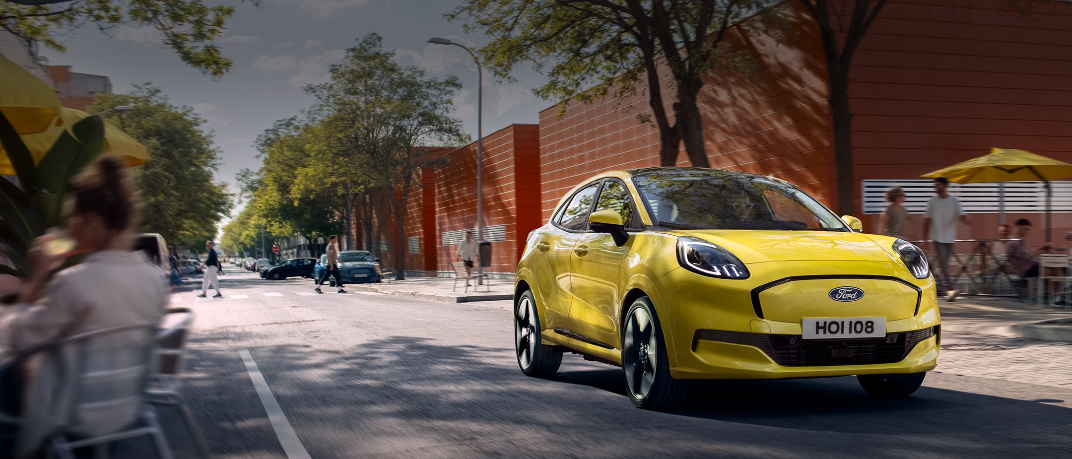 Front view of a yellow electric Ford Puma Gen-E® driving along a city road. Front view of a yellow electric Ford Puma Gen-E® driving along a city road.