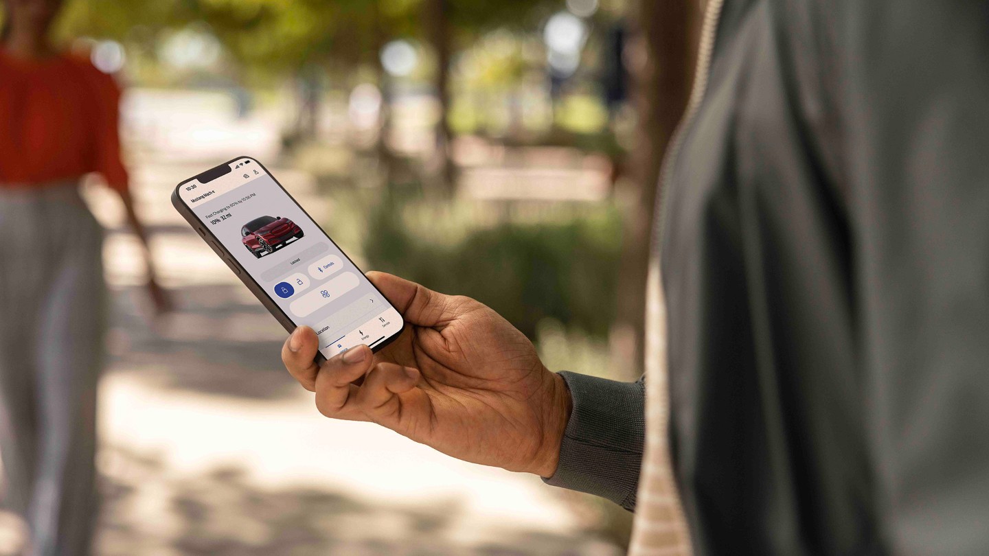 L’application FordPass. Un homme regarde son smartphone. Une Ford Focus couleur bleue en arrière-plan.