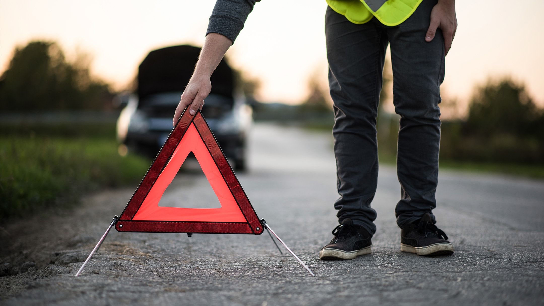 Une personne dispose un triangle de panne rouge, car un véhicule est immobilisé sur le bord de la route.