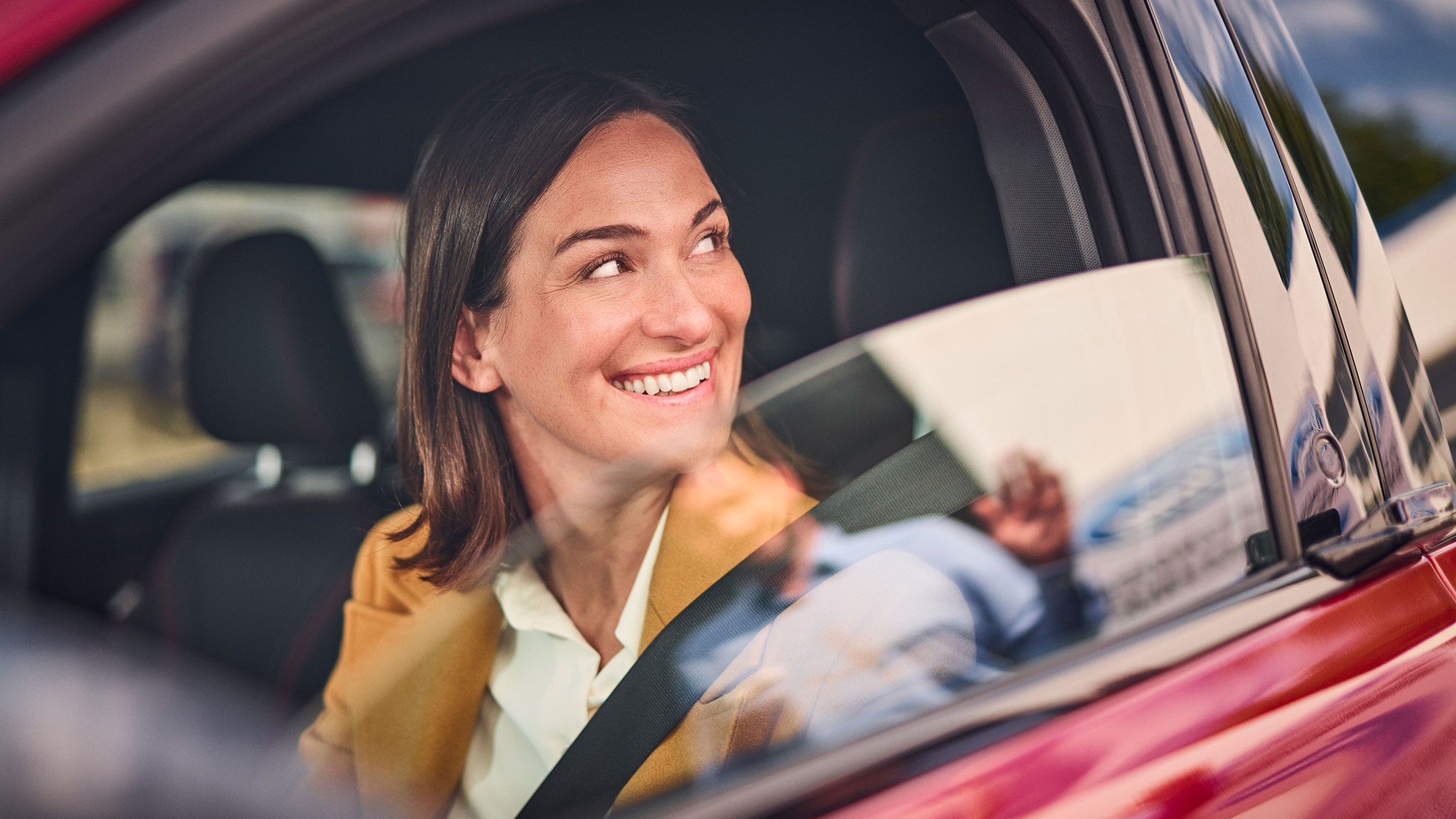 Une femme souriante, assise dans un véhicule Ford rouge.