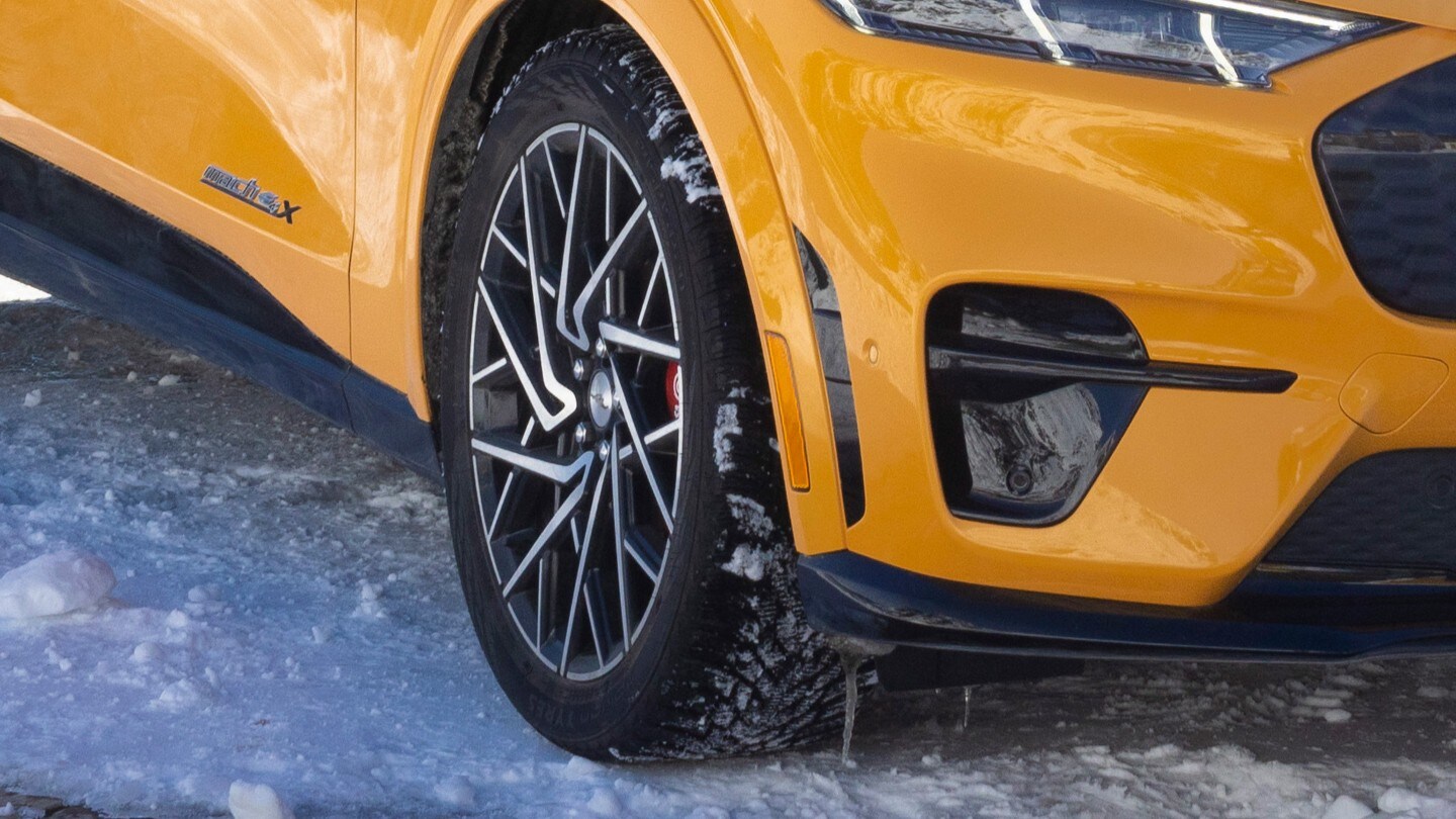 Gros plan sur la roue avant et l’aile d’un véhicule jaune vif – vraisemblablement une Ford Mustang Mach-E – parqué sur une surface enneigée. Gros plan sur la roue avant et l’aile d’un véhicule jaune vif – vraisemblablement une Ford Mustang Mach-E – parqué sur une surface enneigée.